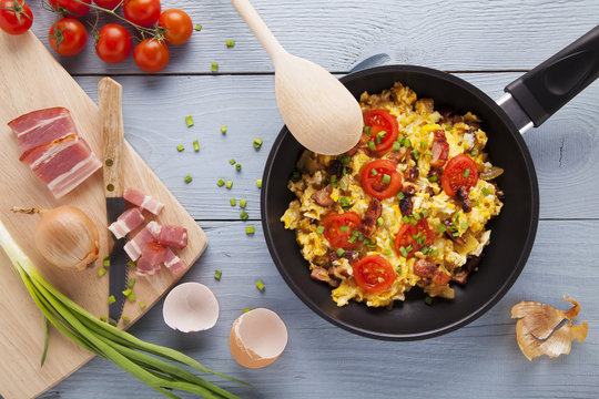 Scrambled eggs in a pan with bacon, onion and tomatoes sprinkled