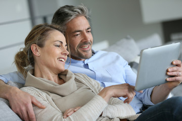 Mature couple relaxing in sofa and using digital tablet
