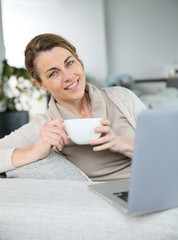 Mature woman relaxing with cup of coffee in front of laptop