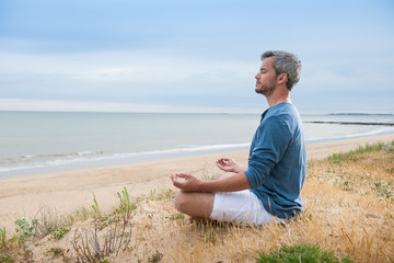 Naklejka na ściany i meble An attractive man is sitting face to the ocean in lotus position