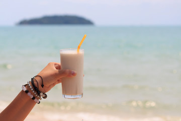 Female hand holding milk shake with tropical sea view background