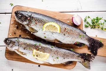 two raw trouts on cutting board with thyme, lemon and red onion