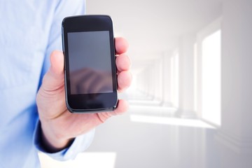 Composite image of businessman showing his smartphone to camera