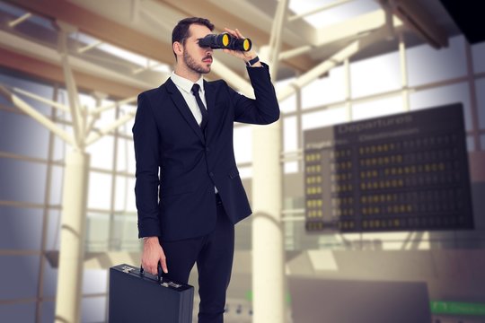 businessman holding a briefcase while using binoculars