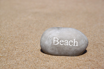 Fototapeta na wymiar one stone pebbles with the word beach over sandy beach