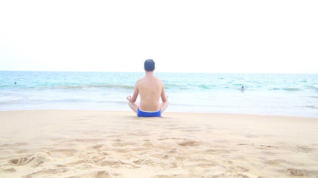 Man meditating on sandy beach in the tropics