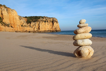 stack of pebble on sandy beach with cliff in the background