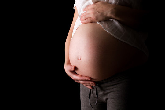 pregnant woman caressing her belly with black background