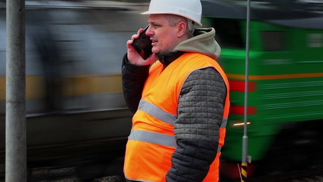 Railway employee talking on cell phone near the passing train