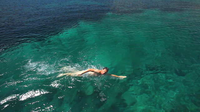 Man swimming in mediterranean close to sailing boat