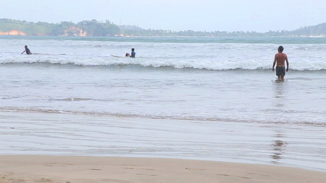 WELIGAMA, SRI LANKA - MARCH 2014: View of the ocean in Weligama with people enjoying the waves. The term Weligama literally means "sandy village" which refers to the area's sandy sweep bay.