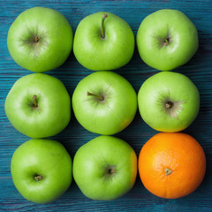 Green apples and one orange on old wooden table