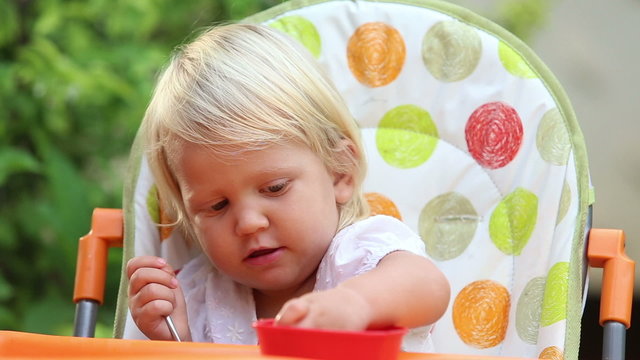 little girl sits in chair eats fruit and tries to feed mother	