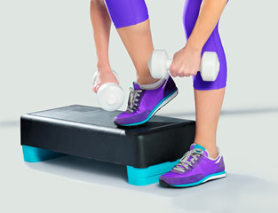 Woman in violet sneakers and sportswear with dumbbells on aerobi