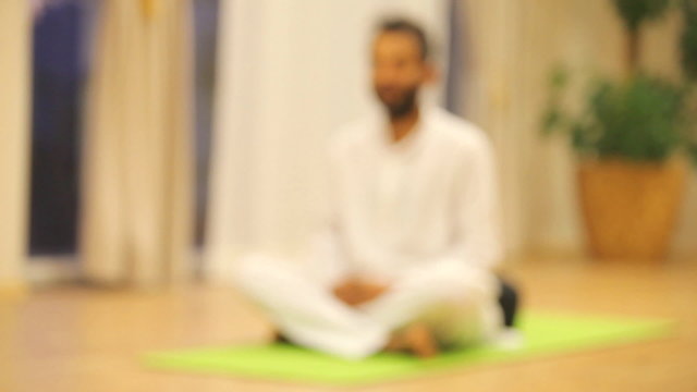 Indian man sitting on green mat and practicing yoga