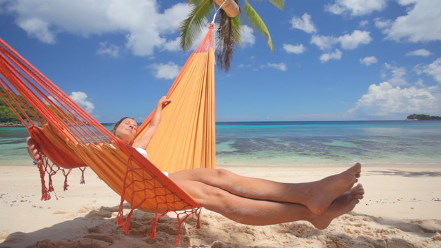 woman in bikini enjoying nap in hammock on sandy beach
