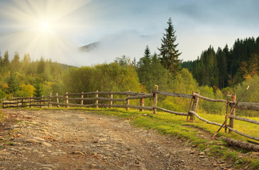 Fototapeta na wymiar Landscape in a mountain valley: road and wooden fence.