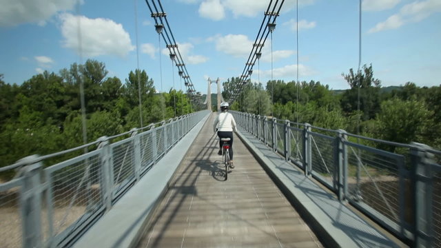 Slow motion - Woman cycling on road over suspension bridge
