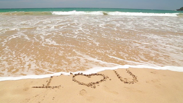 Ocean wave covering words I love you written in sand on beach