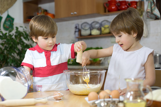 Cute Twins Making Cream For Cake in Glass Bowl at Kitchen Table