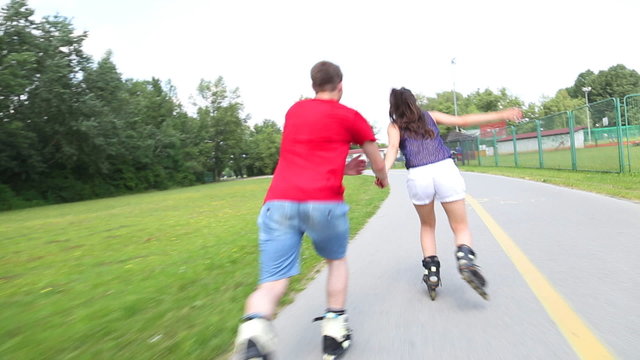 Young woman and man rollerblading and performing in park on a beautiful warm day, holding hands.