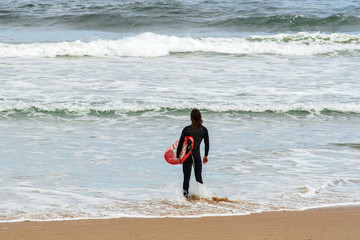 Surfer steht im Wasser und blickt auf die Wellen
