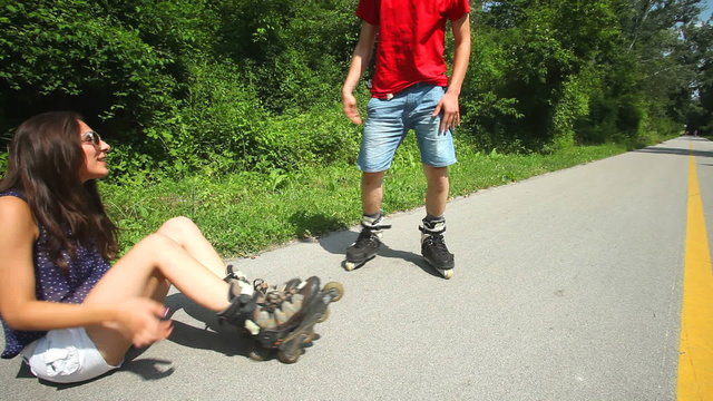 Young woman and man sitting on track, putting their rollerblades on their feet.