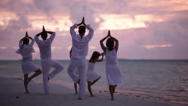 family of six doing yoga at sunset on a beach
