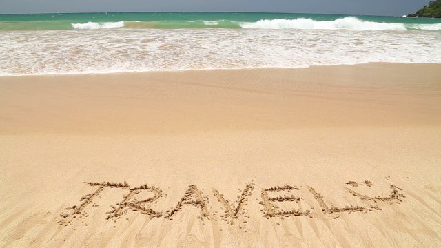 Ocean wave covering word travel written in sand on beach