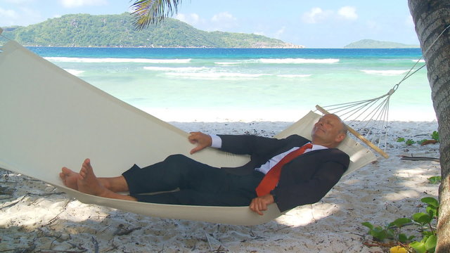 senior businessman relaxing in hammock on tropical beach