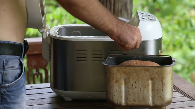 man takes container out of breadmaker and puts on table	