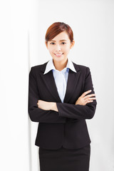 young businesswoman leaning against white wall in office