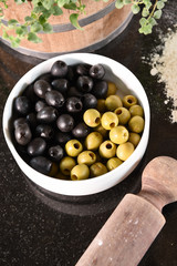 green and black olives in white bowl and ingredients for pizza