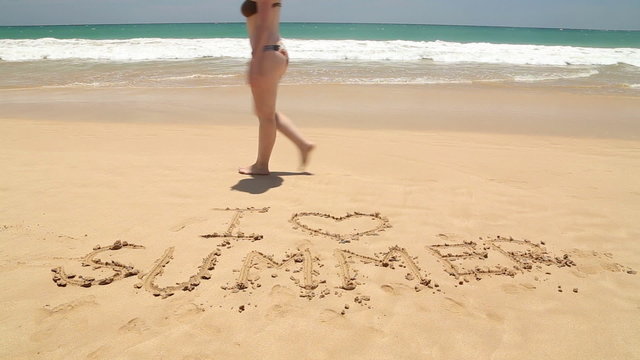 Girl walking in front of words I love summer written in sand on beach