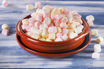 Colorful small marshmallows on blue wooden background.