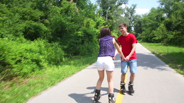 Young woman and man rollerblading on a sunny day in park, holding hands.