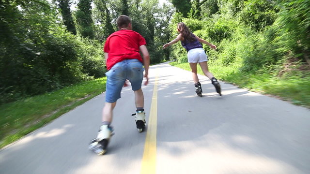 Young woman and man rollerblading and performing in park on a beautiful warm day, going fast