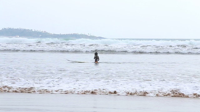 WELIGAMA, SRI LANKA - MARCH 2014: The view of a surfer in the ocean in Weligama. The term Weligama literally means "sandy village" which refers to the area's sandy sweep bay.