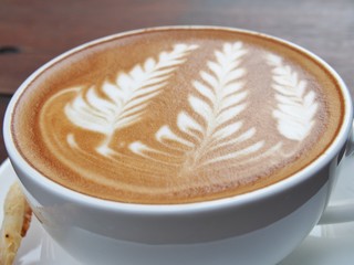 Latte art coffee and biscuit stick on the wooden desk.
