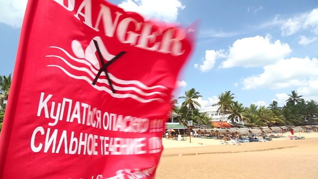 HIKKADUWA, SRI LANKA - FEBRUARY 2014: View of a red flag with warning sign flying on the wind. Waves on Hikkaduwa beach can be dangerous in this time of year.