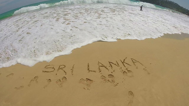 Slow motion of view of waves washing onto beach over writing in the sand Sri Lanka