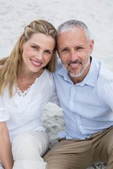 Obraz premium Happy couple sitting on the sand and looking at the camera
