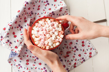 Hands holding hot chocolate with marshmallows in cup