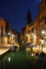 Night channel with boats and tower silhouette in Venice