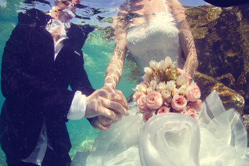 Bride and groom holding hands underwater