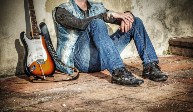 man and guitar leaning against a wall