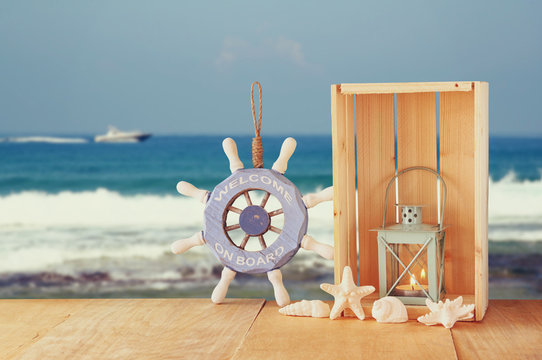Old nautical wood wheel and shells on wooden table over sea back