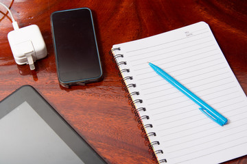 Tablet with notebook on wooden table and pen