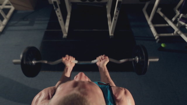 Muscular man doing exercise for biceps with a barbell in the gym