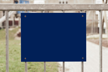 Ein dunkelblaues unbeschriftetes Schild an einem Metallzaun